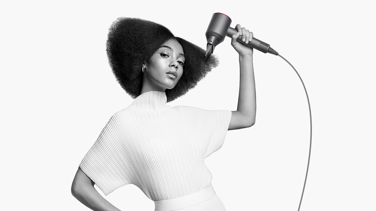 Woman holding Dyson Supersonic hair dryer with wide tooth comb attachment